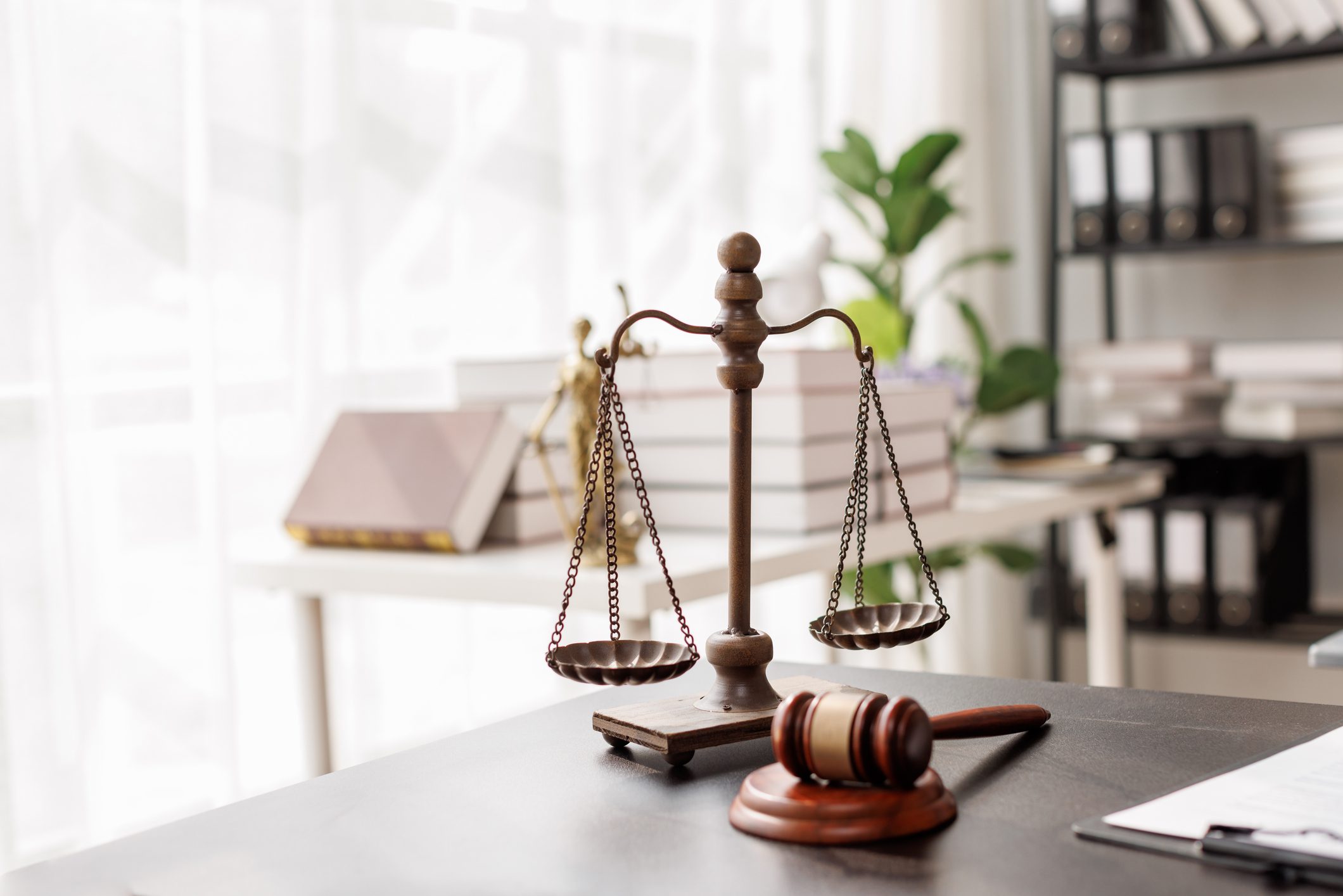 A wooden justice scale and gavel on a desk in a bright office.